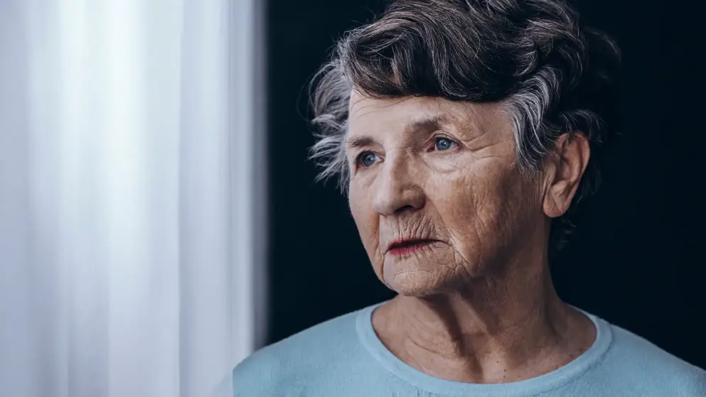 Older woman with Alzheimers staring out of a window, confused