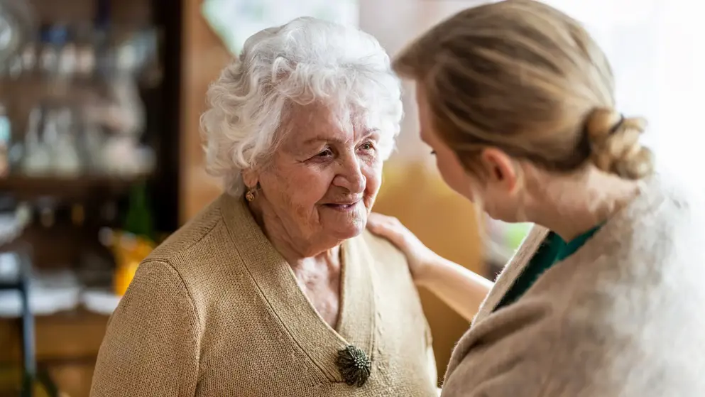 Woman with dementia smiling while being assisted by carer