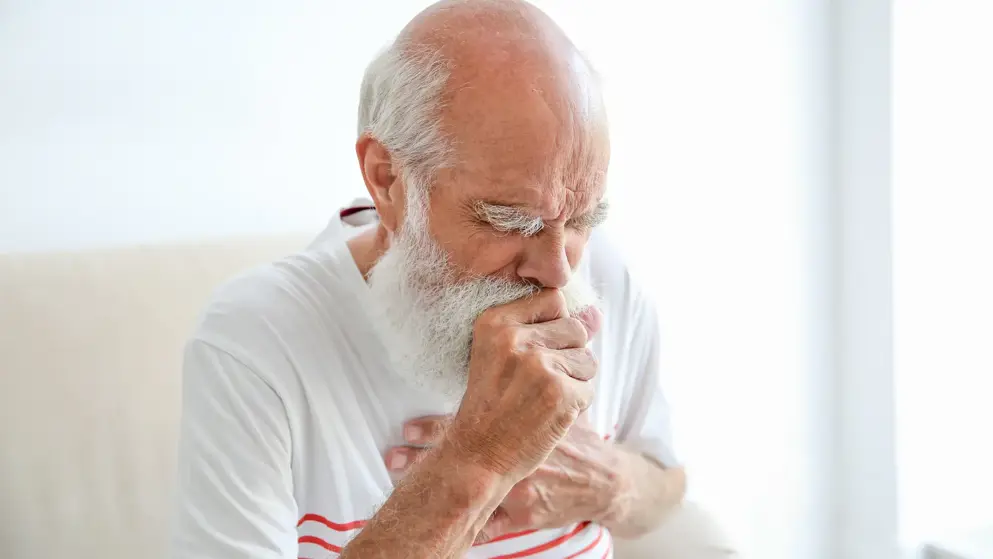 Older man with bald head and white beard coughing and covering his mouth due to regurgitation and/or reflux