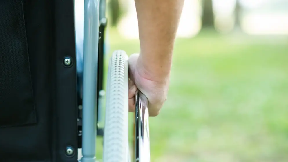 A hand on the wheel of a wheelchair, pushing forward; multiple sclerosis